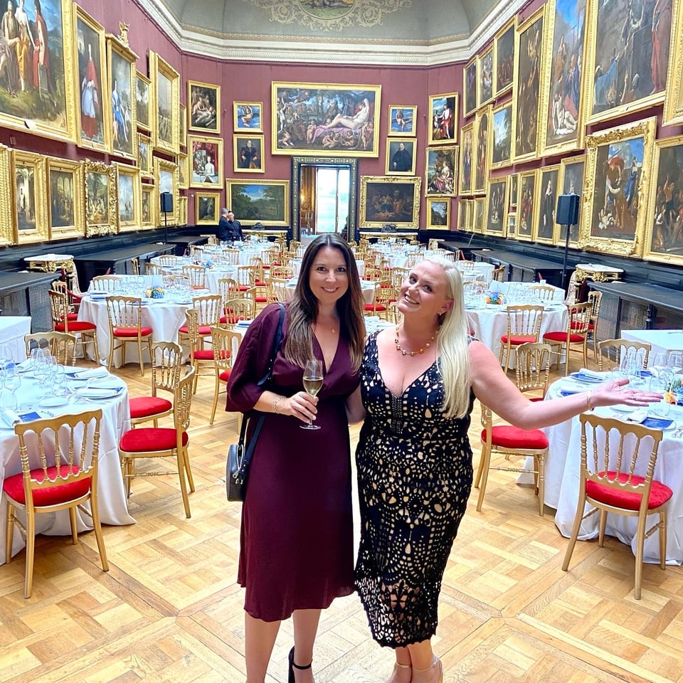 Jennifer and a guest among round dinner tables in the picture-hung gallery of the Château de Chantilly.