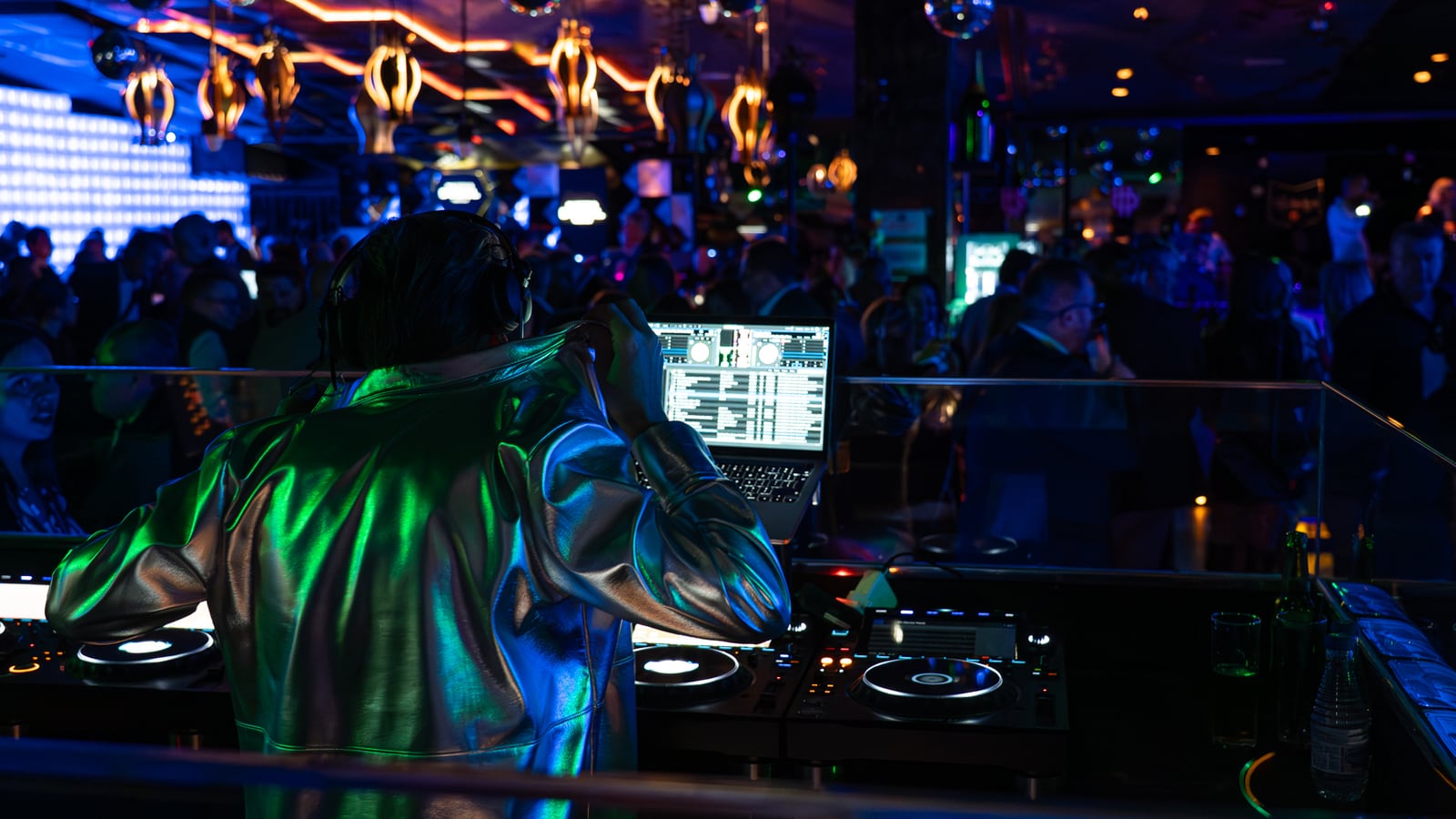 A DJ in an iridescent jacket at the decks under club lights.