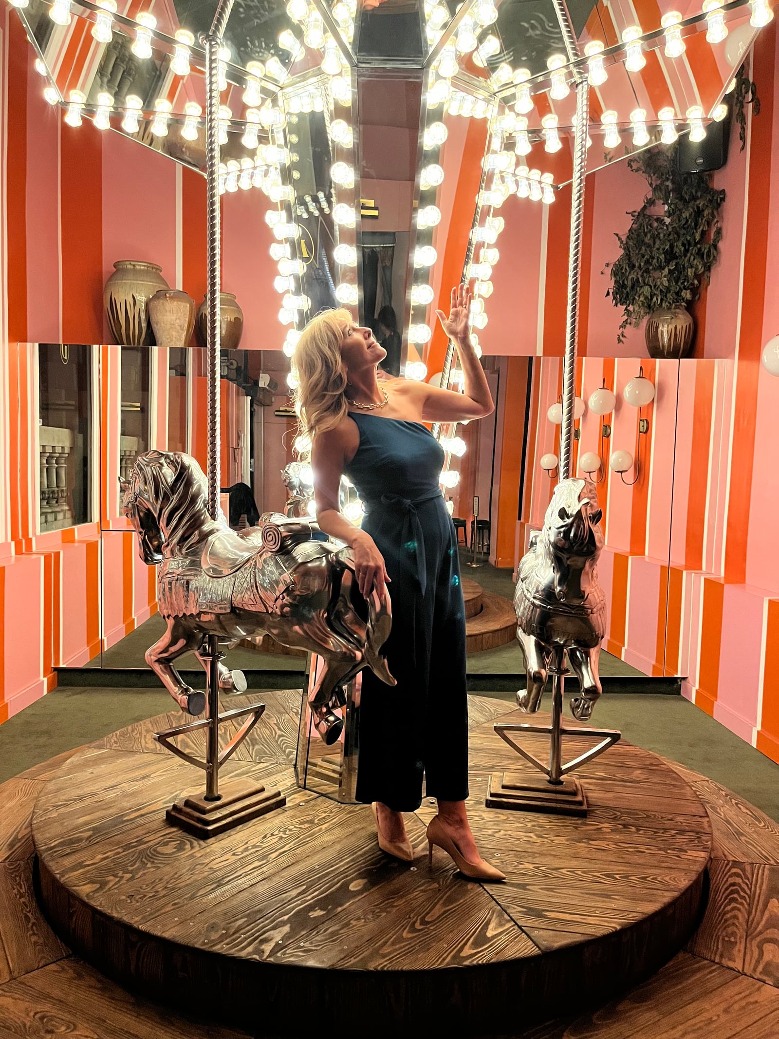 Jennifer beside a fairground carousel horse in an orange-striped room.