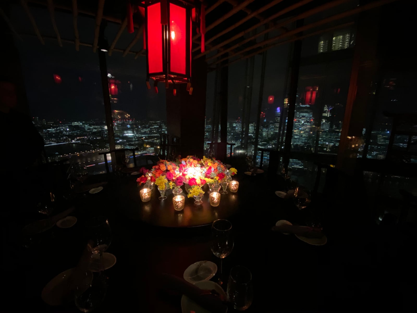 A dark dining room at Hutong with red lanterns and the City of London far below.