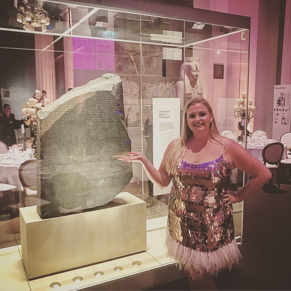 Jennifer in evening dress beside the Rosetta Stone in its display case at the British Museum.