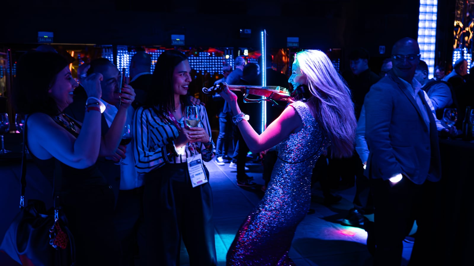 An electric violinist in a sequinned dress playing to guests on a blue-lit dance floor.